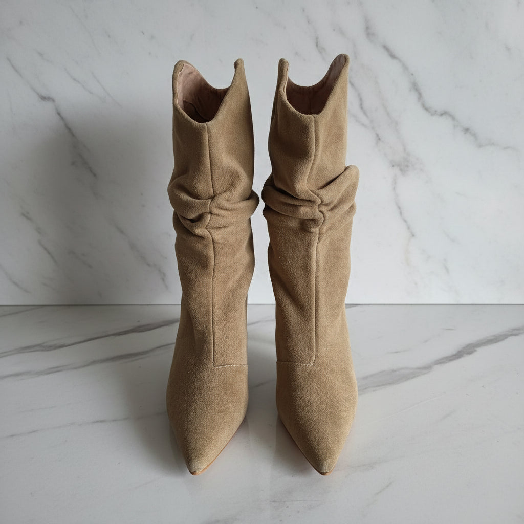 Pair of beige suede boots with pointed toes and tied design on a marble surface