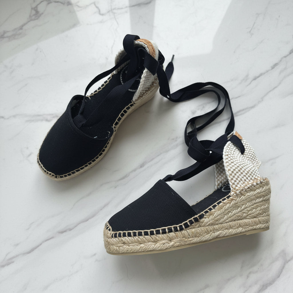 Black wedge sandals with jute sole on a white marble surface