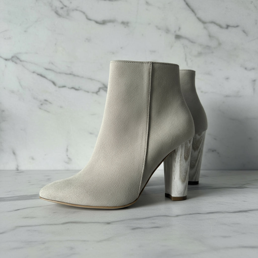 Pair of beige suede ankle boots with metallic heel on a light gray background
