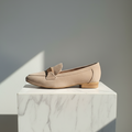Beige loafer shoe on a marble pedestal with a gray background