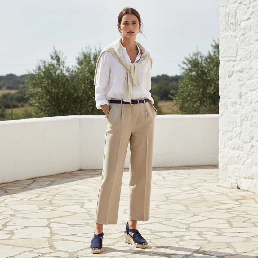 Woman in a white shirt, beige cardigan, and beige pants standing on a stone patio with a scenic background.