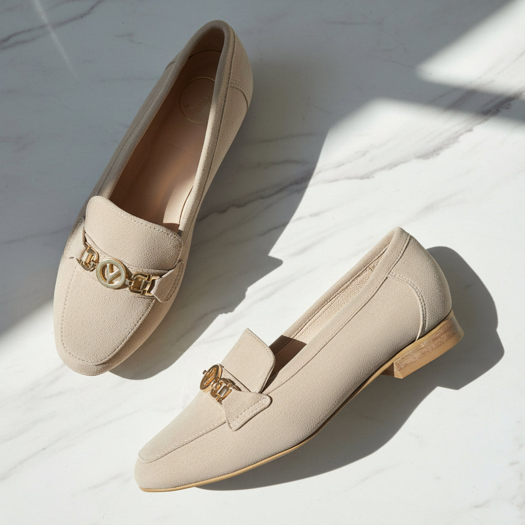 Pair of beige loafers with gold accents on a light marble background