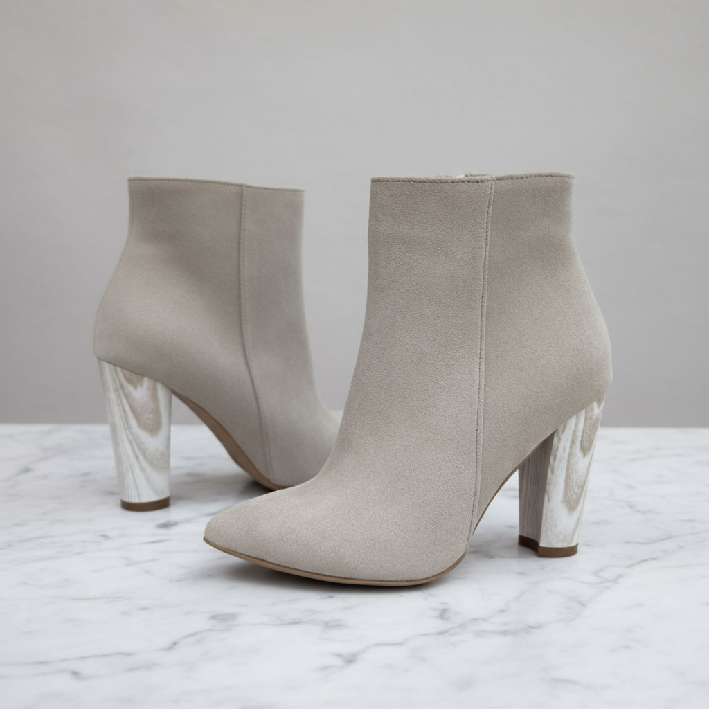 Pair of beige high-heeled ankle boots on a metal grid background