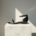 Black sandal with a checkered strap on a marble pedestal against a gray background