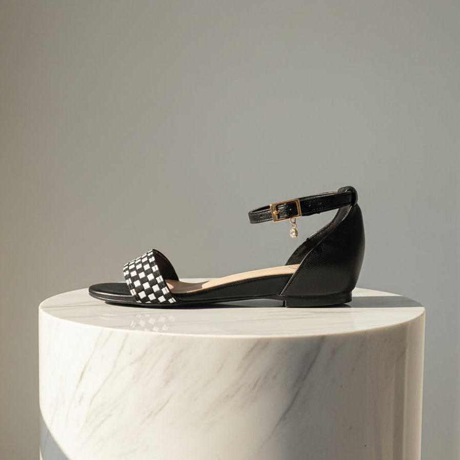 Black sandal with a checkered strap on a marble pedestal against a gray background