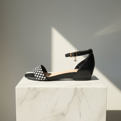 Black sandal with a checkered strap on a marble pedestal against a gray background