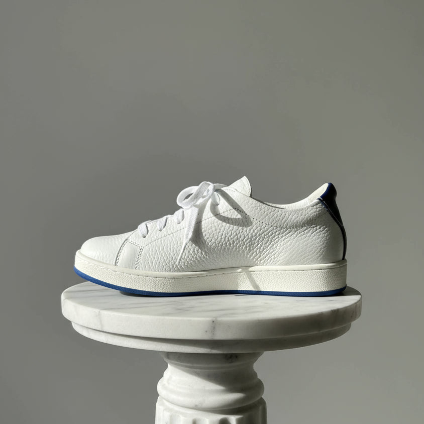 White textured sneaker with blue sole on a gray background
