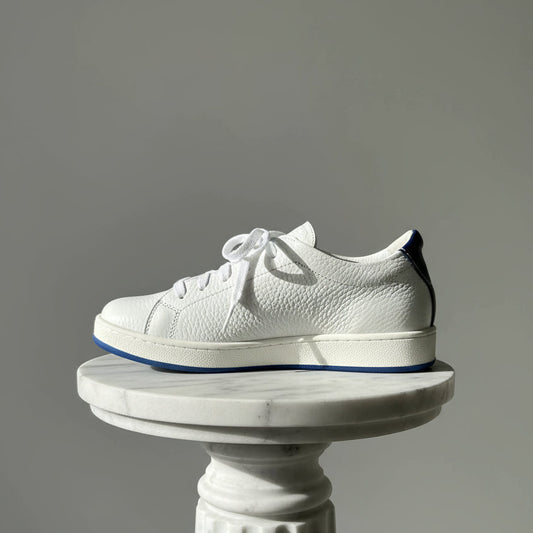 White textured sneaker with blue sole on a gray background