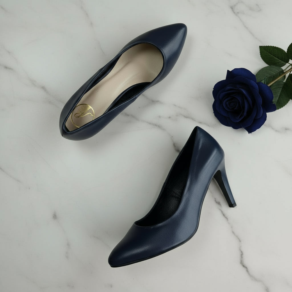Pair of navy high-heeled shoes on a marble surface with green leaves.