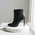 Black high-heeled ankle boot on a marble platform with a neutral background