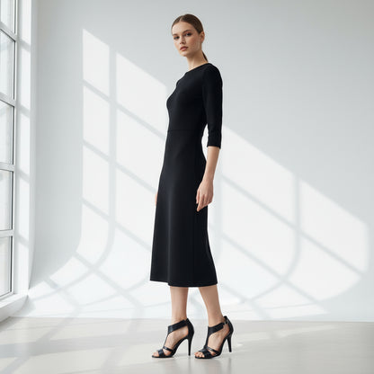 Woman wearing a black dress standing in a bright room with large windows.