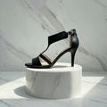 Black leather sandal on a white marble pedestal against a light grey marble background