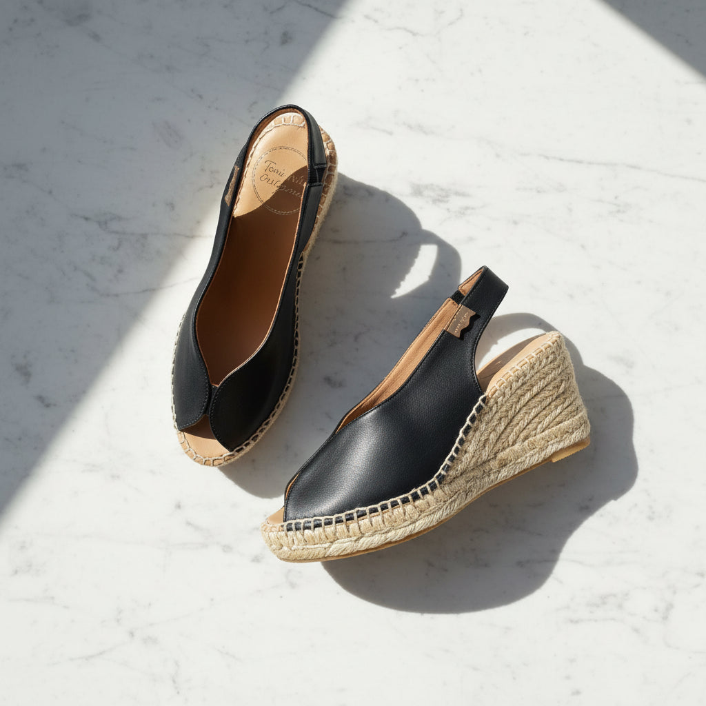 A pair of women's wedge espadrille sandals in navy blue leather with natural jute-wrapped wedge heels, displayed on a light gray textured surface.