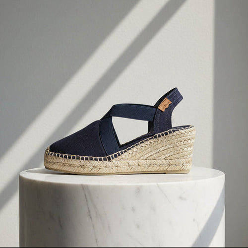Navy espadrille sandal on a white marble pedestal with a gray background
