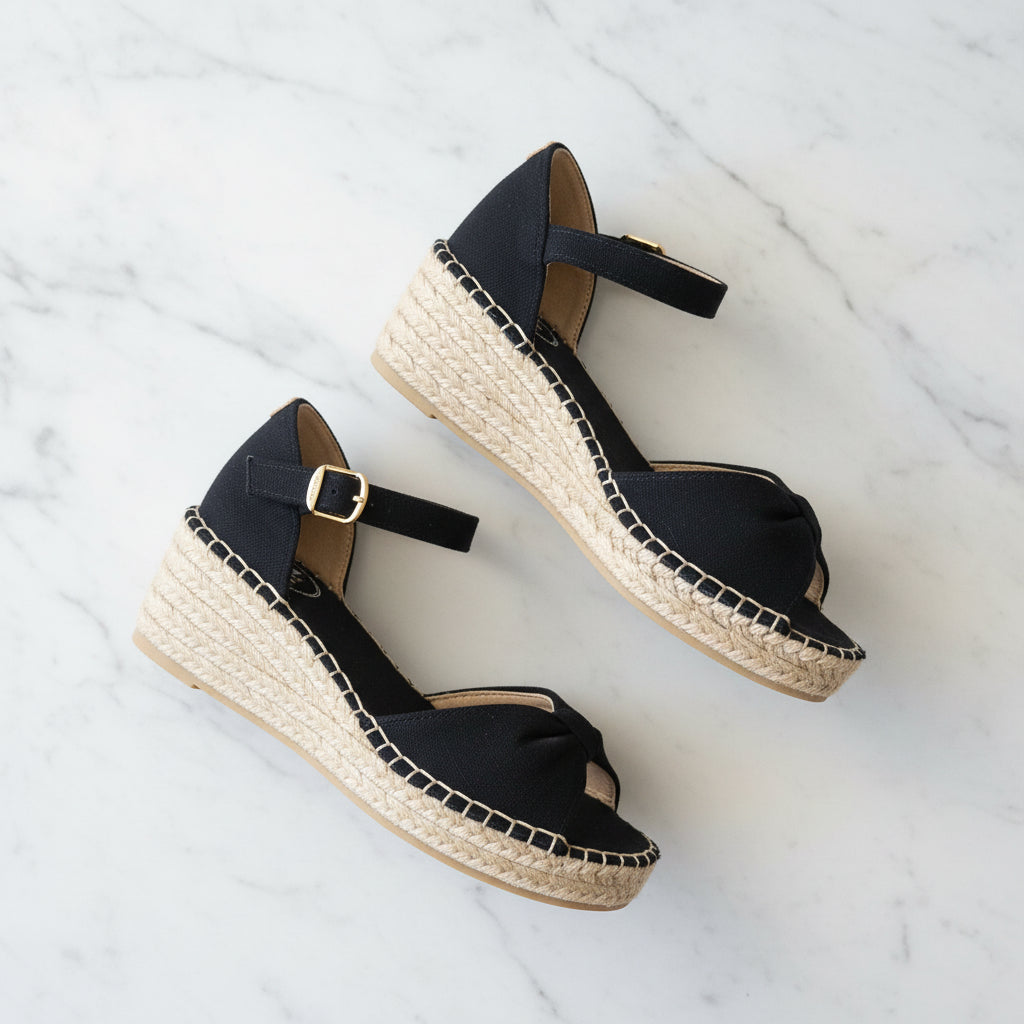 Black wedge sandals with espadrille sole on a white marble background