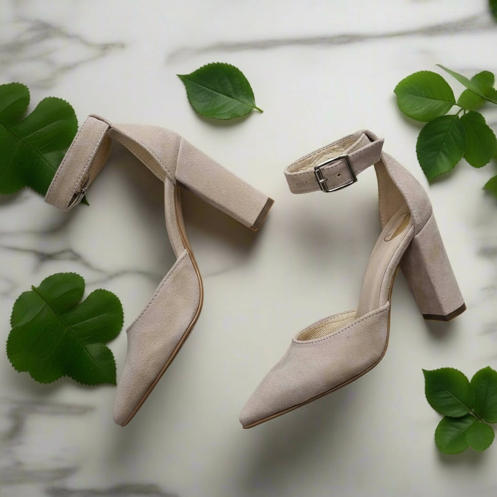 Pair of beige high-heeled shoes on a light background with green leaves.