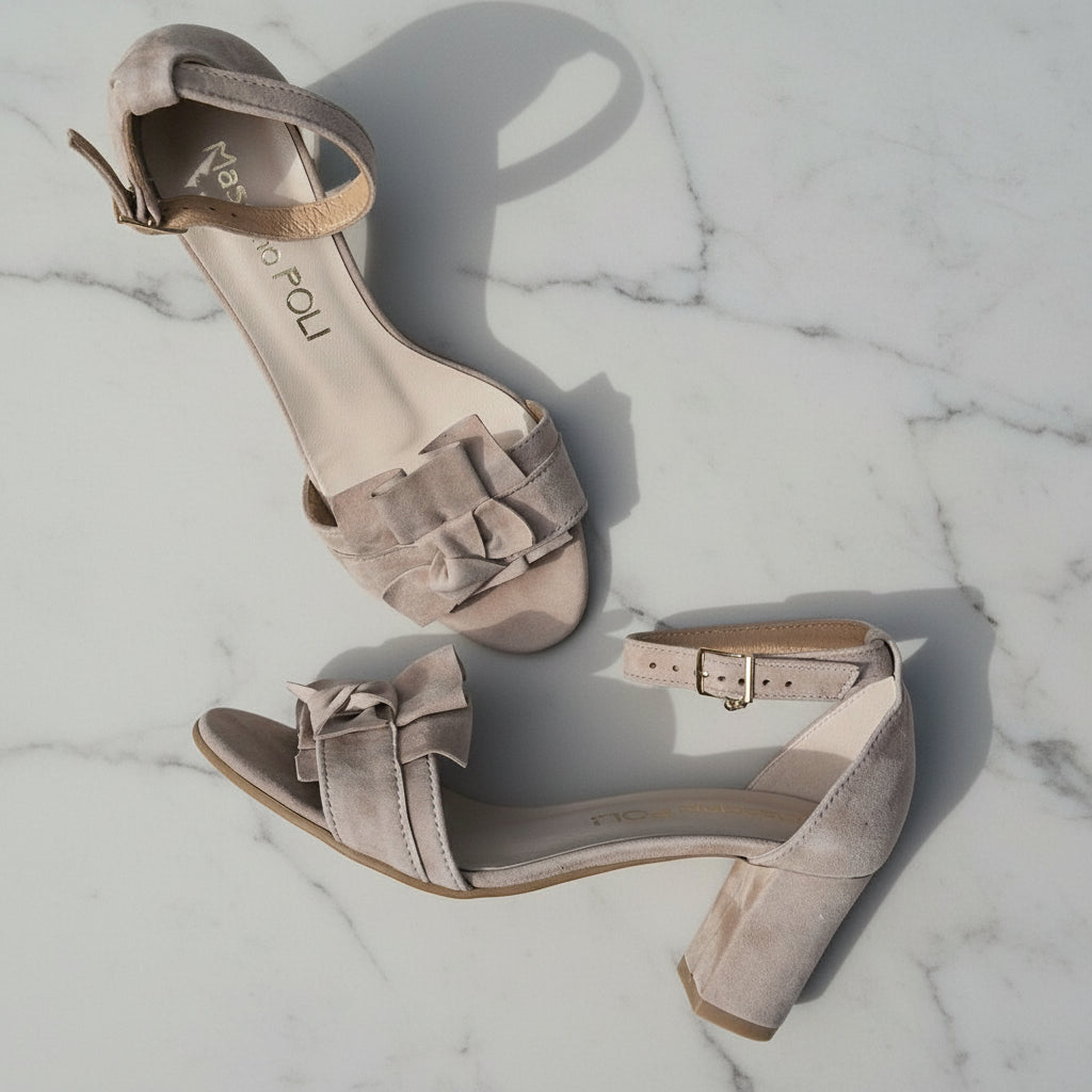 Pair of beige high-heeled sandals with bow details on a marble surface