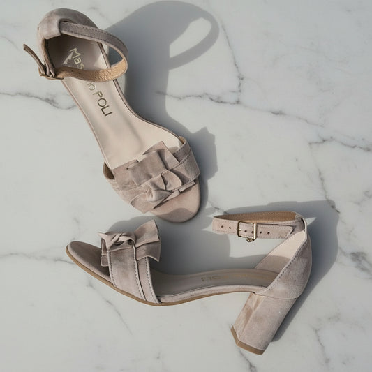 Pair of beige high-heeled sandals with bow details on a marble surface
