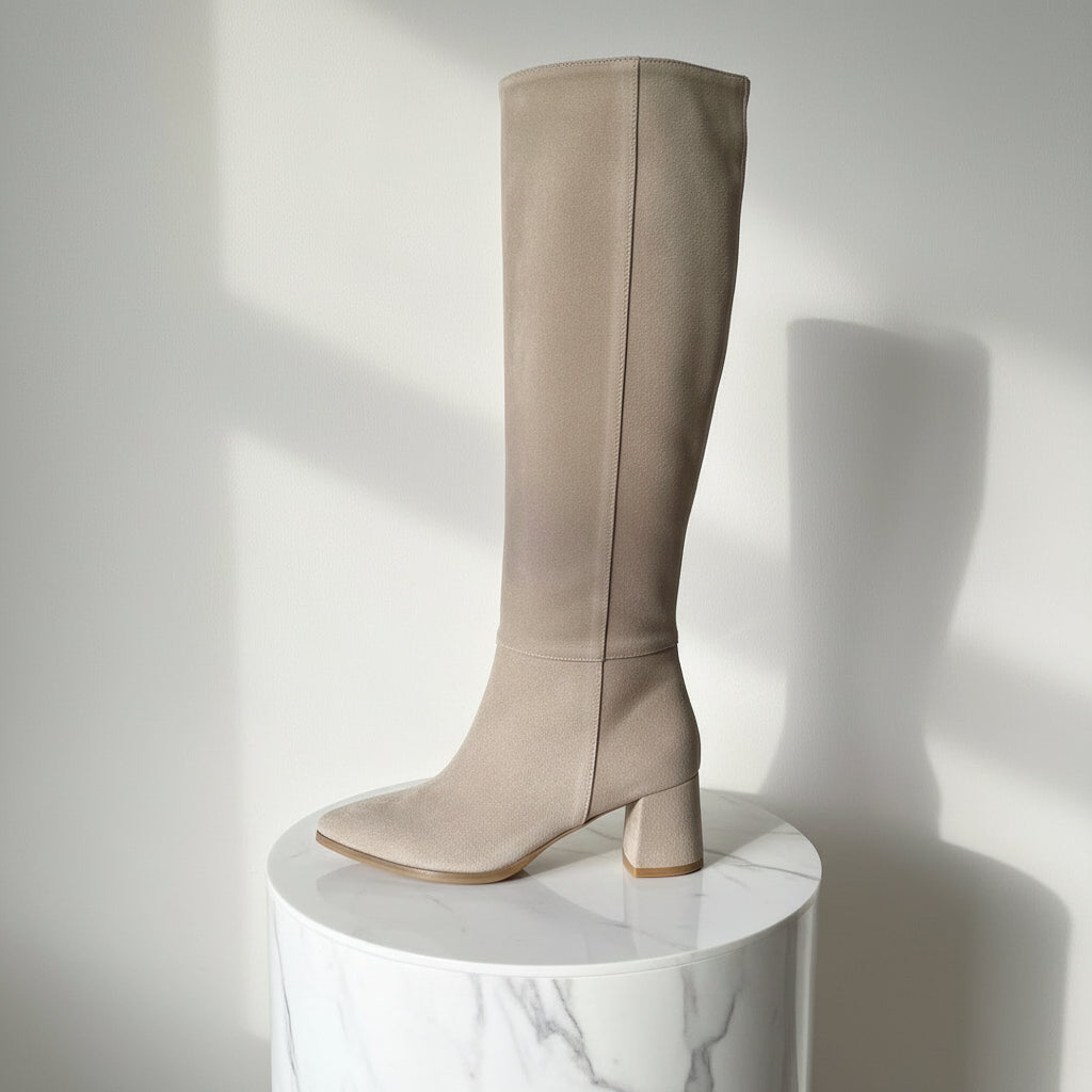 Beige knee-high boot on a white pedestal against a light gray background
