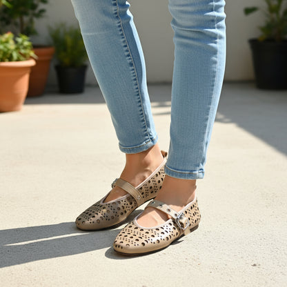 Person wearing beige leather mary jane flats and light blue jeans on a concrete surface with plants in the background.