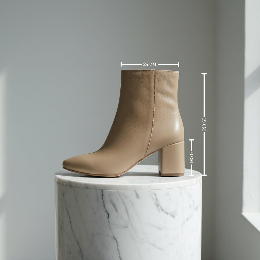 Beige leather pointed toe ankle boots elevated on a marble stand with size measurements.