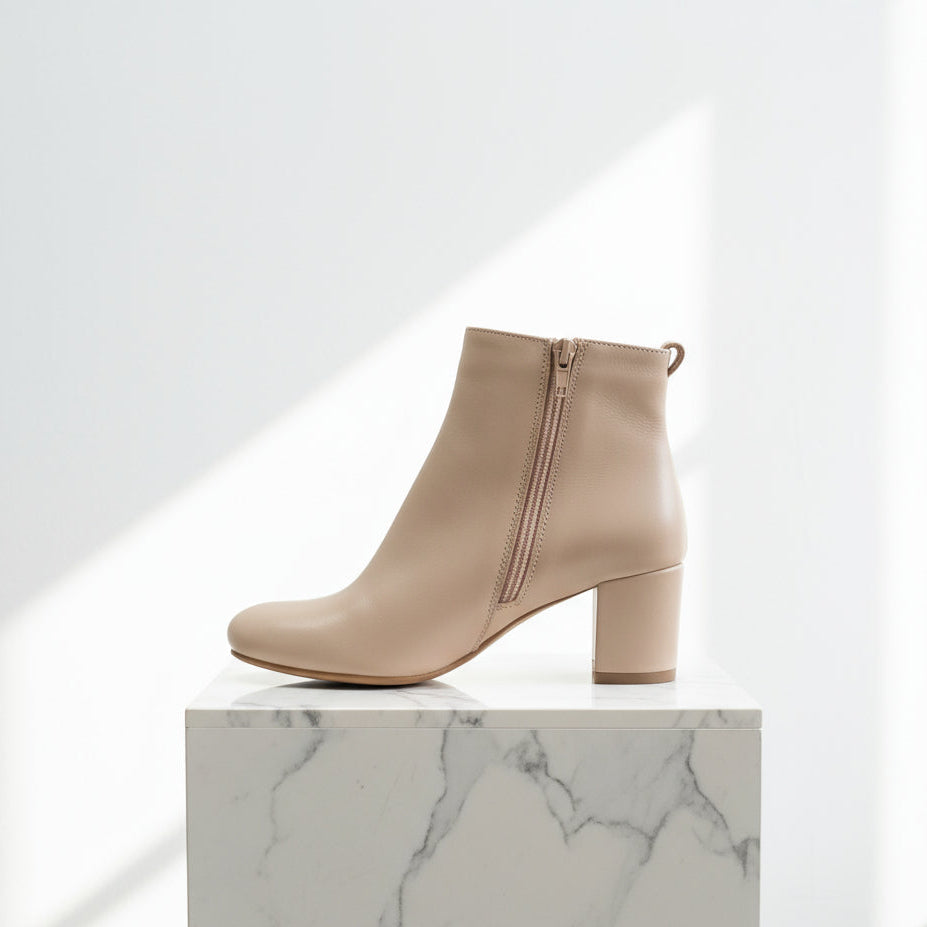 Beige ankle boot on a marble surface with a white background