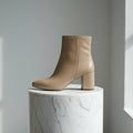 Beige ankle boot on a marble pedestal against a gray background