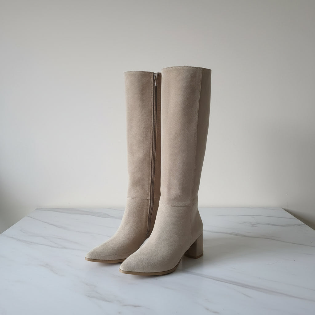 Pair of beige knee-high boots on a light marble surface with a neutral background