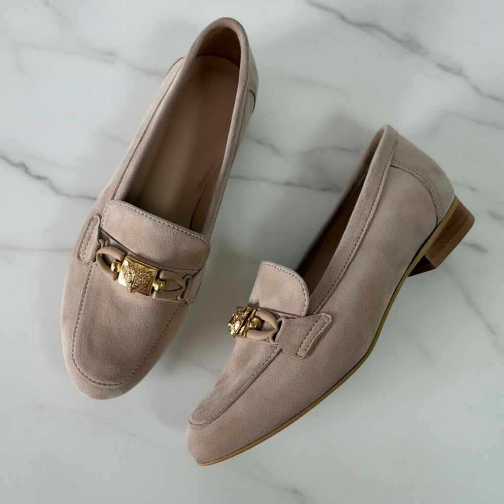 Pair of beige loafers with gold accents on a light gray background