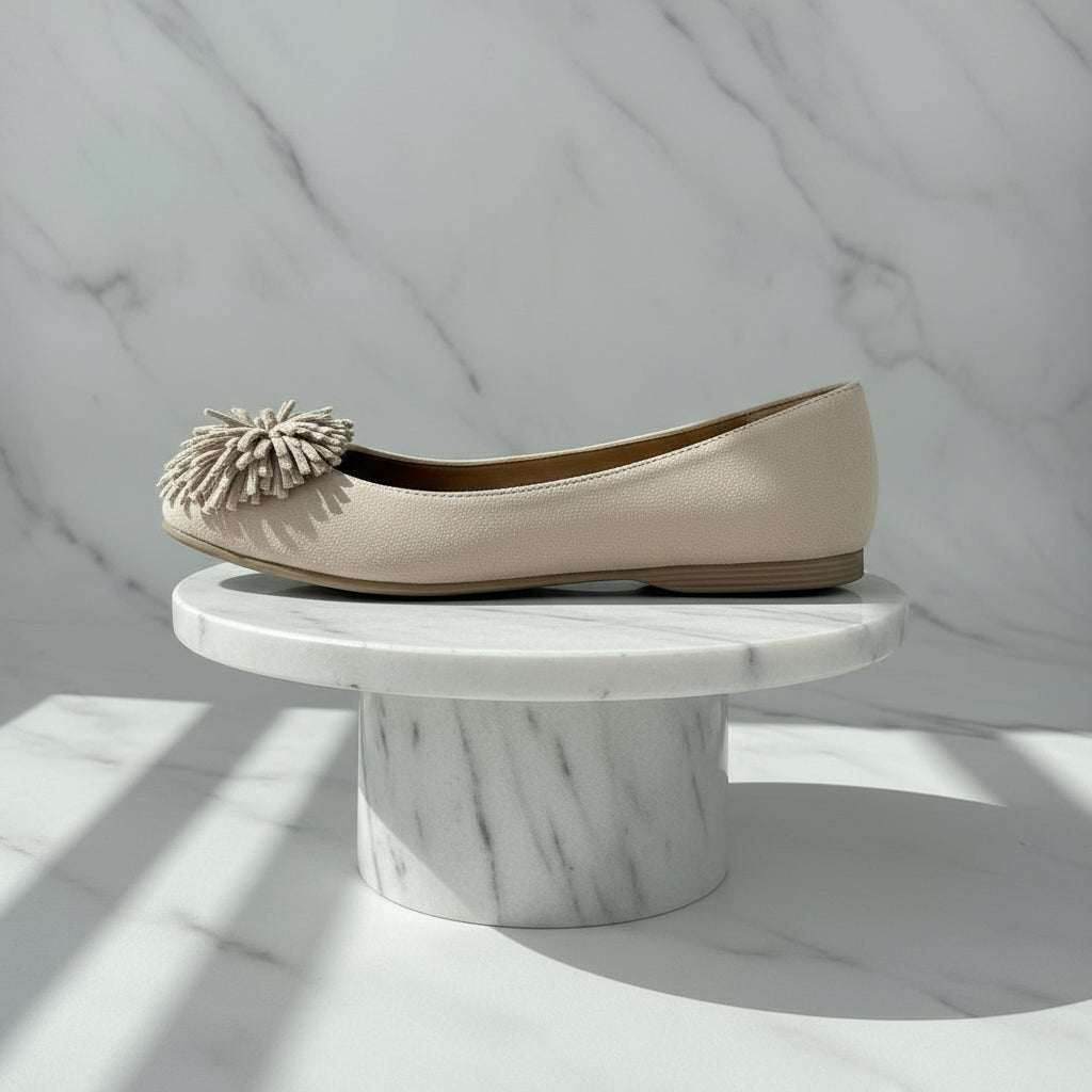 Pair of beige suede shoes with pom-pom details on a light gray background