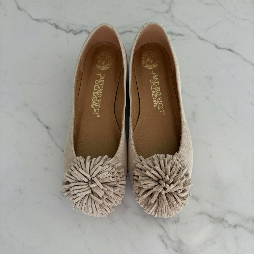 Pair of beige flats with pom-pom details on a white background