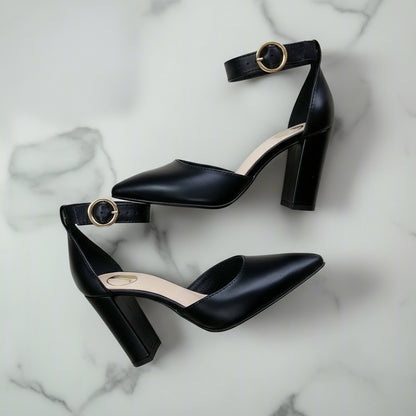 Black leather ankle strap heels with chunky block heel and gold buckle worn, side view.