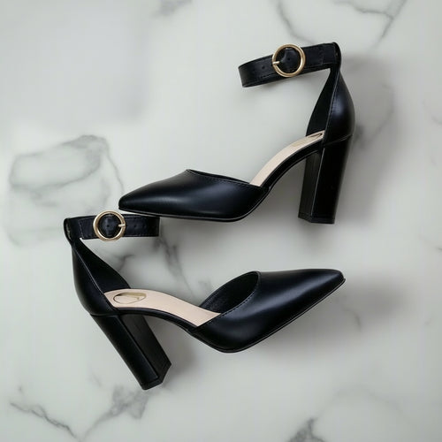 Black leather ankle strap heels with chunky block heel and gold buckle worn, side view.