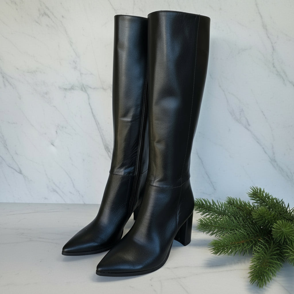Pair of black knee-high boots on a white surface with a blurred indoor background
