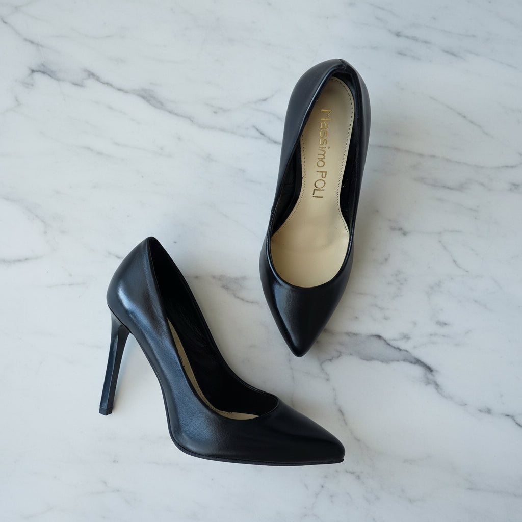 FELICIA black leather stiletto heels angled in mid-air on marble background