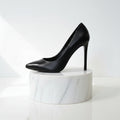 Black leather high-heeled shoe on a white marble stand against a white background