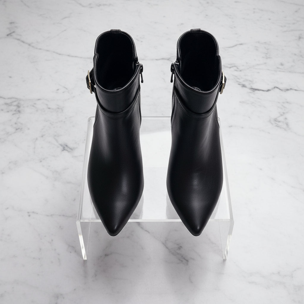 Pair of black ankle boots on a clear stand against a marble background