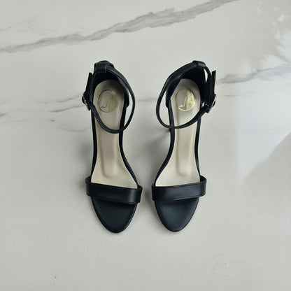 Black high-heeled sandals on a marble surface with green leaves.