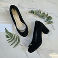 Top view of pair of black suede block heel shoes with silver buckle detail and cushioned insole on grey surface