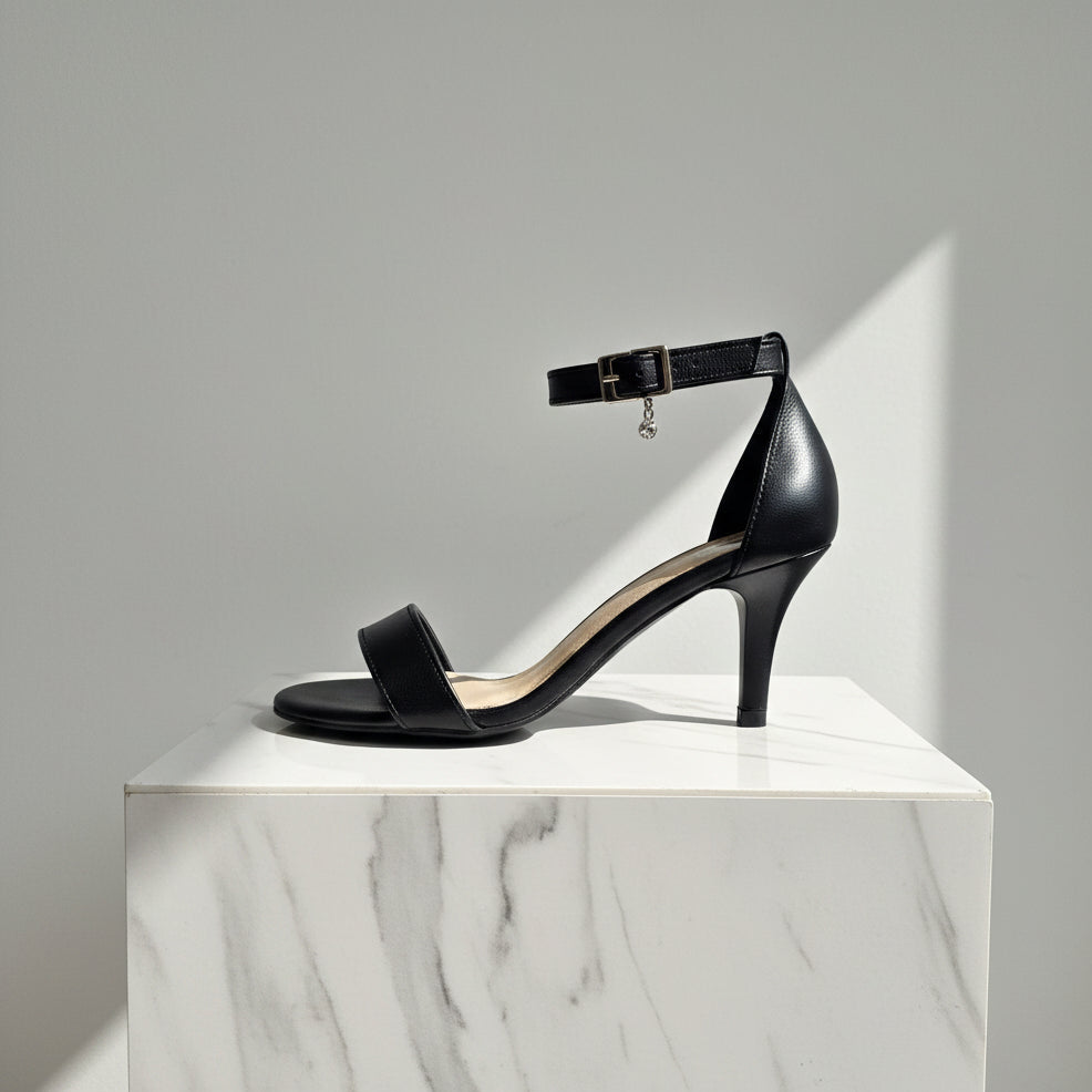 Black high-heeled sandal on a white marble pedestal against a gray background