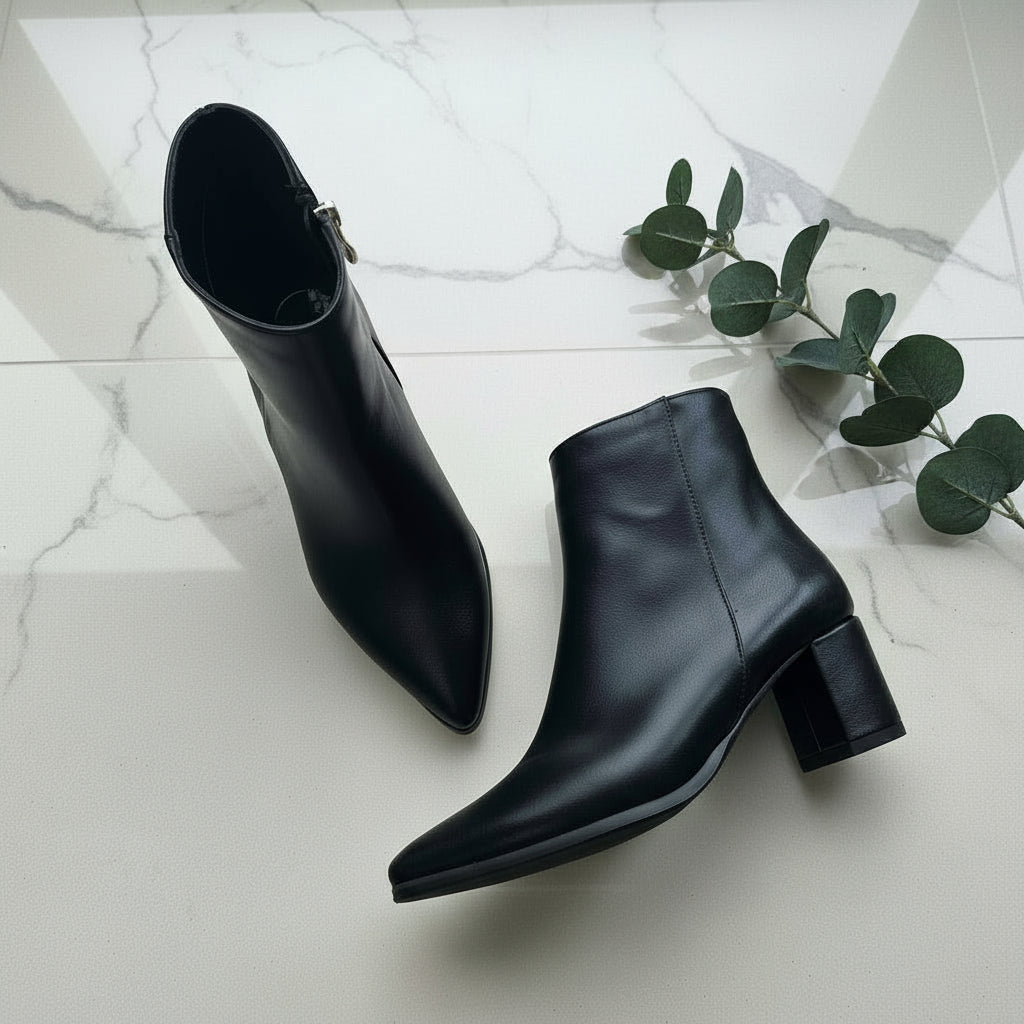 Black leather boots on a marble floor with a branch of eucalyptus.