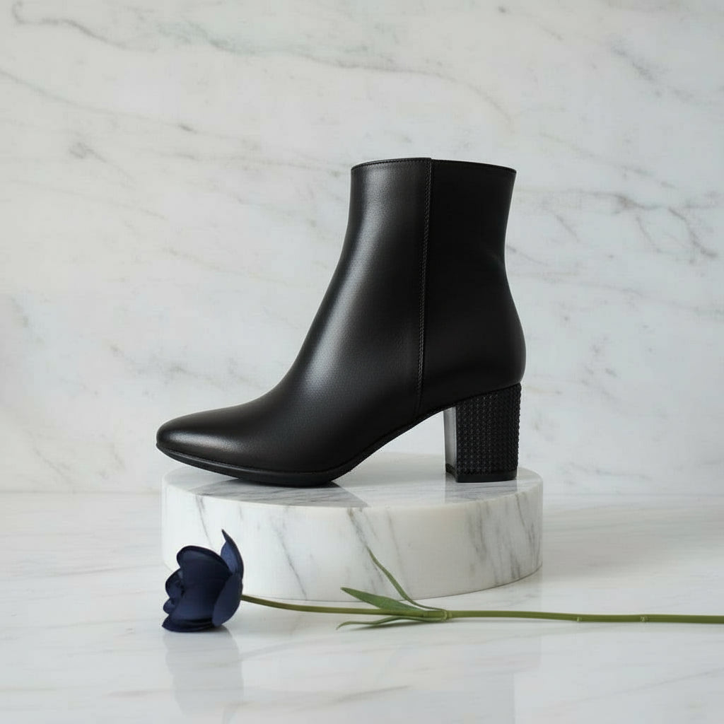 Black ankle boots on a marble stand with a white marble background