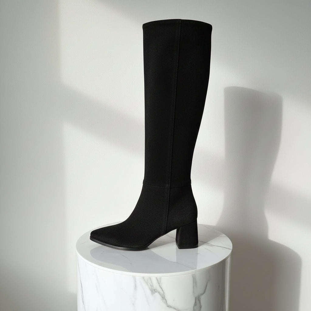 Black knee-high boot on a white pedestal against a light gray background