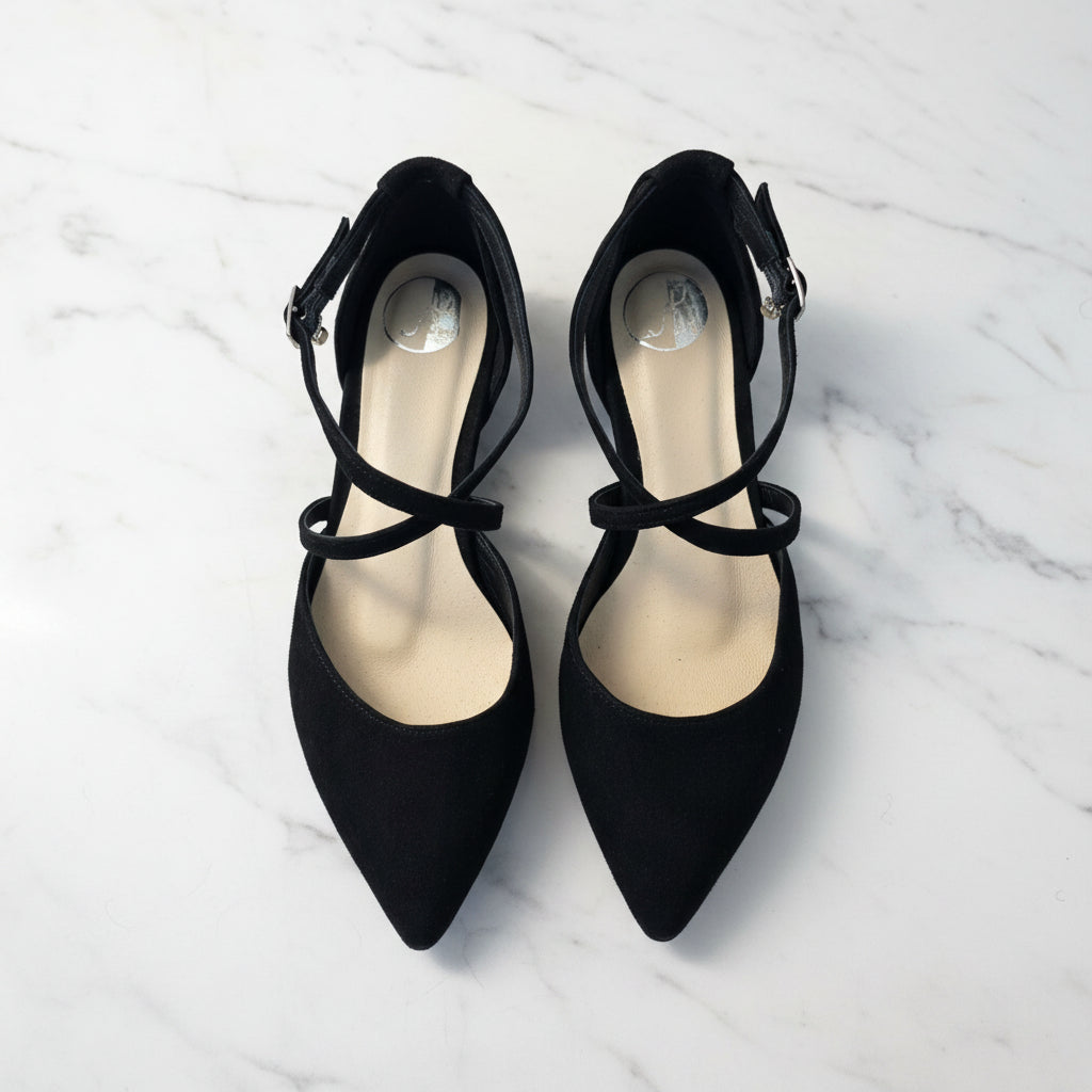 Pair of black pointed-toe shoes with strappy design on a white marble background