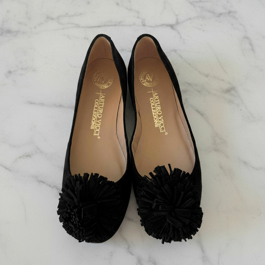 Black shoes with pom-pom details on a white background