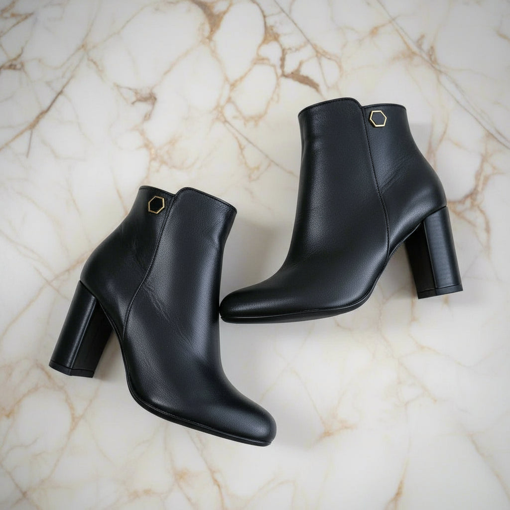 Flat lay of CELIA black leather ankle boots with hex hardware and inner zip.