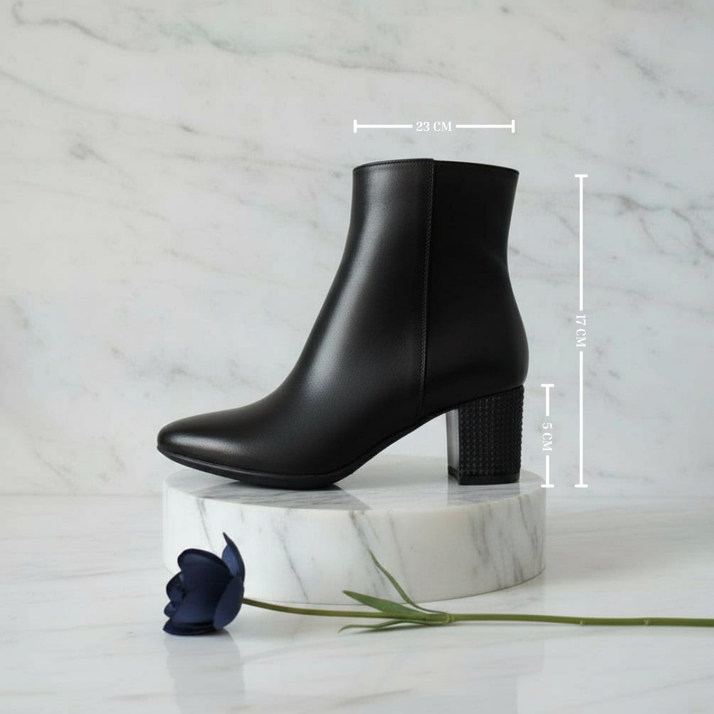 Black ankle boot on a marble stand with measurements indicated, against a marble background.
