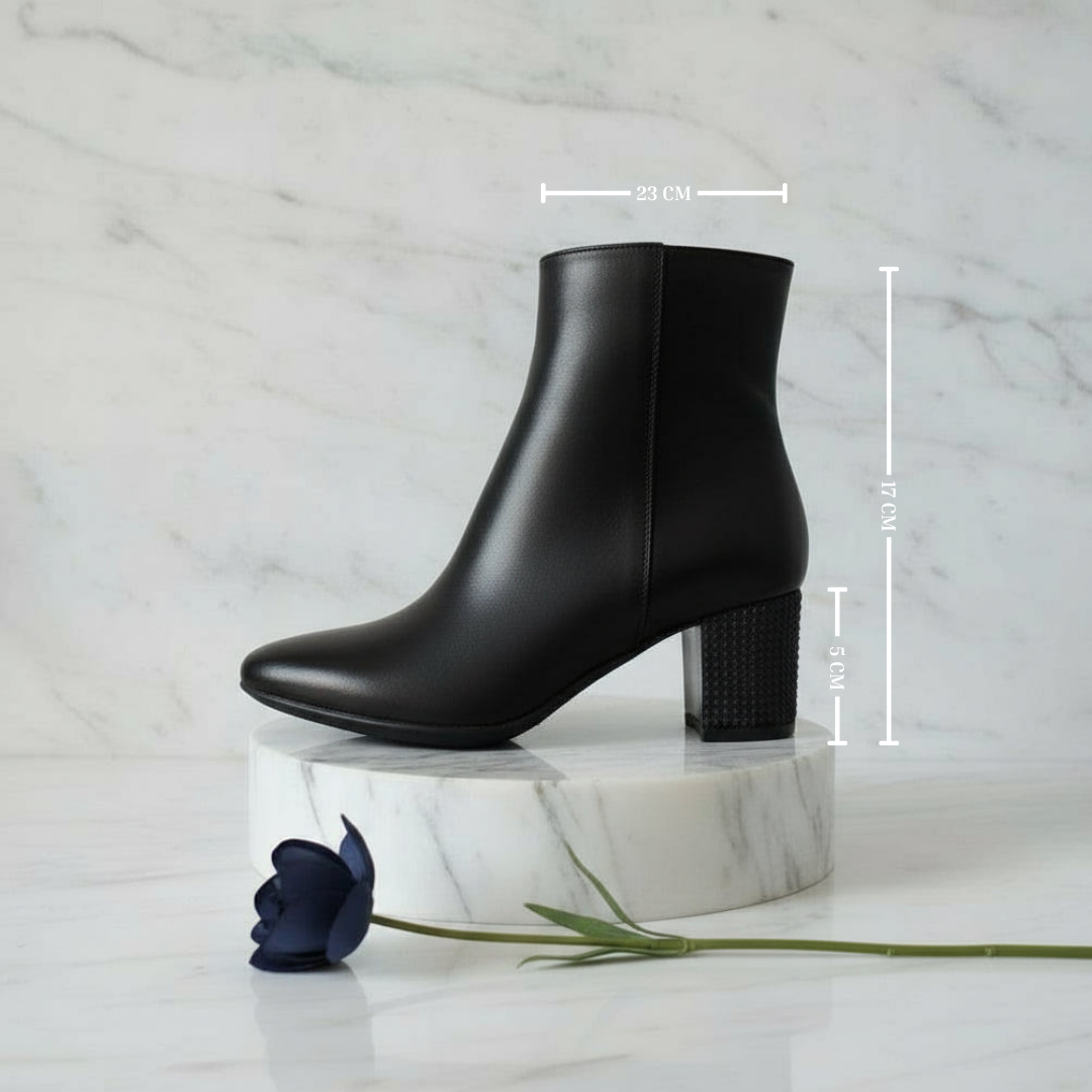 Black ankle boot on a marble stand with measurements indicated, against a marble background.