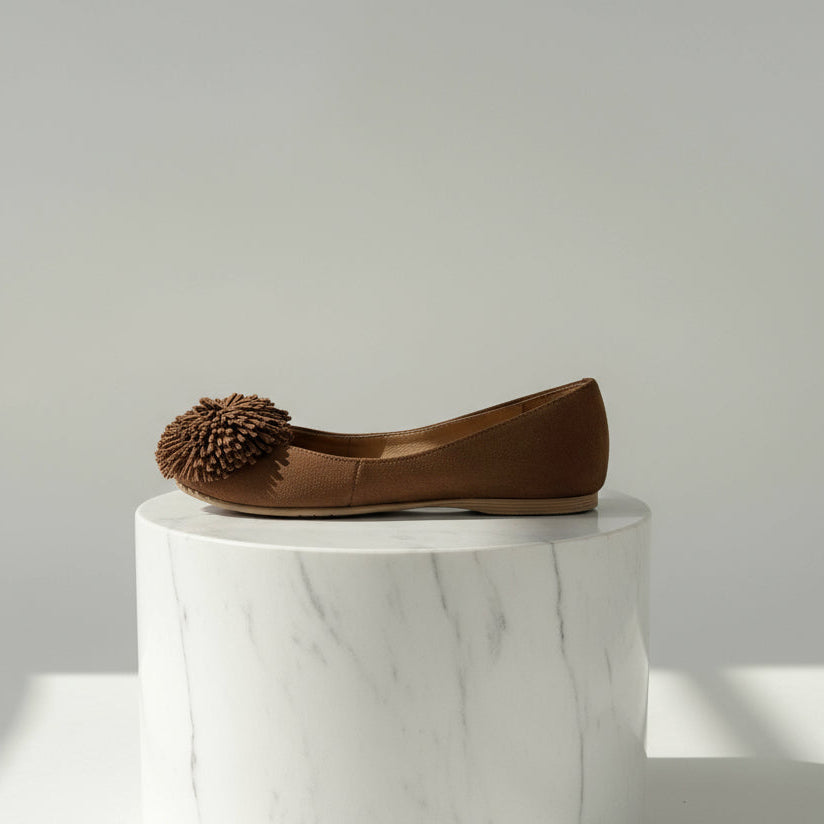 Brown flat shoe with a pom-pom on a white background