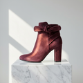 Burgundy suede ankle boot for women with small feet, featuring a decorative bow, rounded toe and block heel, displayed on a white marble pedestal.